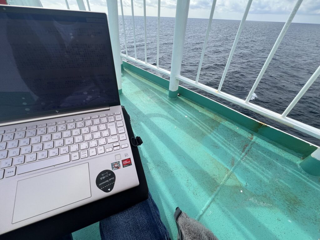 膝の上のPCと、その向こうの海